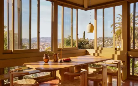 Une salle à manger lumineuse dans une veranda sur terrasse en bois, avec vue panoramique sur la ville et les palmiers.