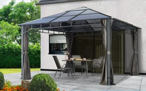 Une tonnelle def. avec table et chaises sur une terrasse pavée, devant une maison blanche et un jardin verdoyant.