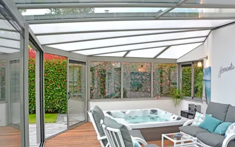 Une **fenêtre de toit veranda** lumineuse abrite un jacuzzi et un coin salon confortable, avec vue sur un jardin luxuriant.
