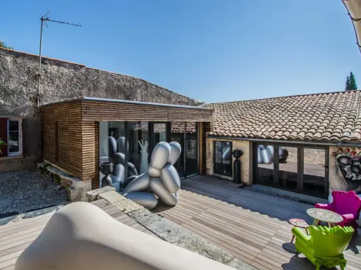 Extension maison ancienne architecte : une cour avec sculptures modernes, mobilier coloré et une extension en bois et verre.