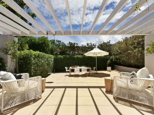 Terrasse couverte avec pergola blanche, mobilier de jardin blanc, table et parasol. Un espace extérieur aménagé, peut-être pour fermer une terrasse couverte sans autorisation.