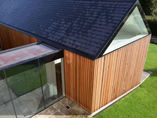 Vue aérienne d'un agrandissement maison sur le côté, avec bardage bois, toit en ardoises et extension vitrée.