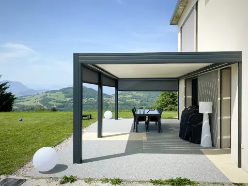 Pergola bioclimatique moderne face à un paysage vallonné. Le vent fort fait onduler les lames du toit, créant des jeux d'ombre et de lumière.