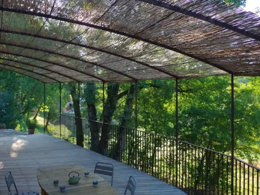 Vue d'une terrasse en bois sous une pergola recouverte de canisse. Le sens de pose de canisse sur pergola offre une ombre naturelle et agréable.