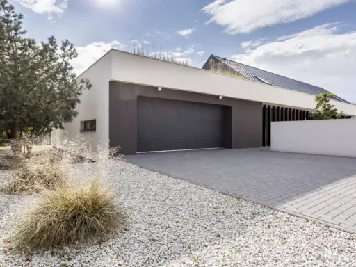 Moderne maison avec agrandissement garage, allée pavée, gravier blanc et végétation.