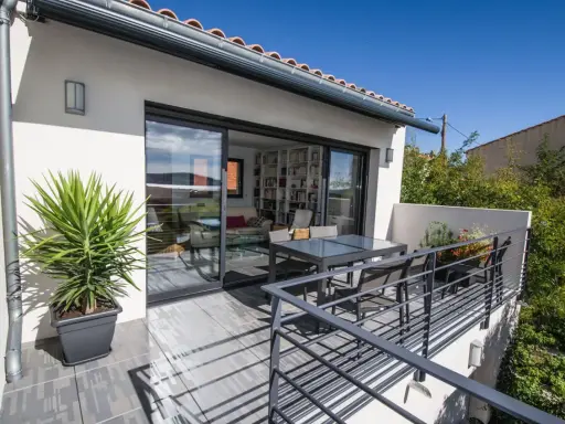 Terrasse sur le toit accessible, avec table et chaises, et une grande baie vitrée donnant sur un salon rempli de livres.