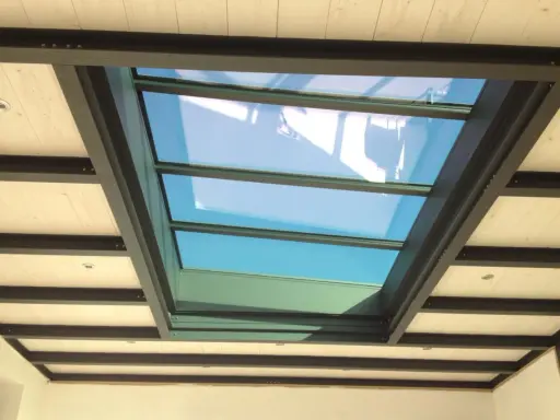Veranda avec un grand puit de lumière vitré, illuminant un plafond en bois et poutres métalliques.