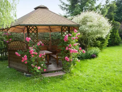Pergola en bois ornée de roses roses, installée dans une pelouse verdoyante. Idéal pour savoir comment fixer une pergola dans l'herbe.