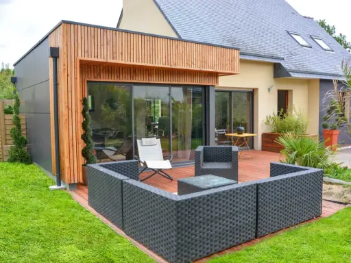 Une extension bois 30m2 moderne avec terrasse en bois, mobilier de jardin et grandes baies vitrées.