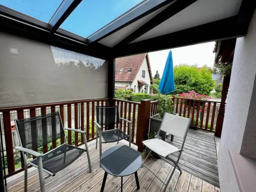 Un petit veranda balcon avec des chaises et une table, offrant une vue sur un jardin verdoyant et une maison.