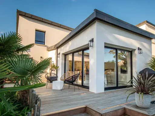 Une extension verrière moderne illumine cette maison ancienne, offrant une vue imprenable sur la terrasse en bois et le jardin luxuriant.