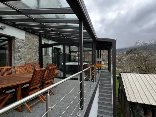 Veranda sur terrasse surélevée avec jacuzzi et table en bois. Vue sur un village et des collines brumeuses.