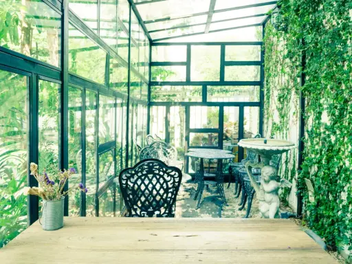 Un charmant jardin d'hiver verrière, avec des tables et chaises en fer forgé, une statue d'ange et une profusion de verdure.