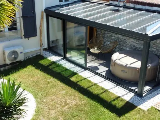 Une **veranda tuile** moderne avec jacuzzi et fauteuils, entourée d'un jardin verdoyant et d'une palme luxuriante.
