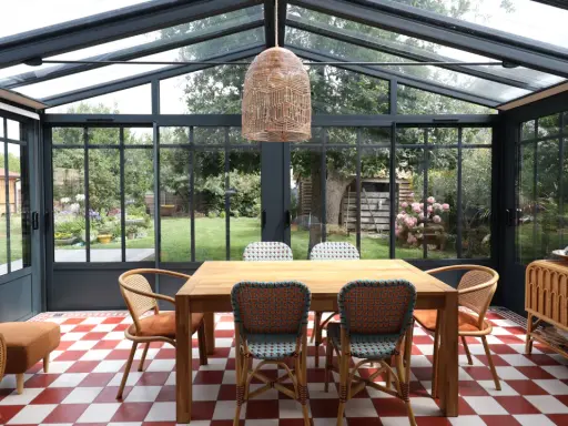 Salle à manger lumineuse dans une véranda extension, avec table en bois, chaises colorées et vue sur le jardin.