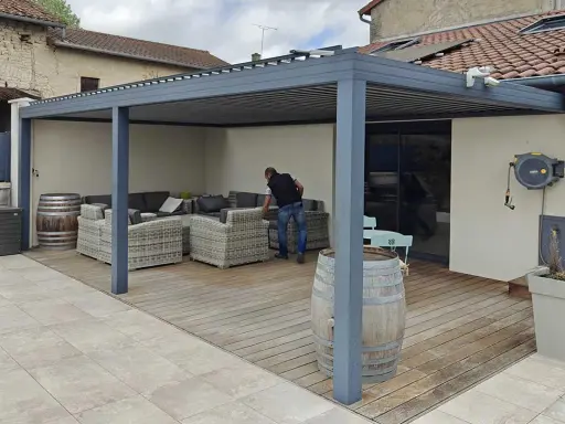 Installation d'un auvent sans permis de construire. Un homme arrange des coussins sur un canapé extérieur sous la structure moderne.