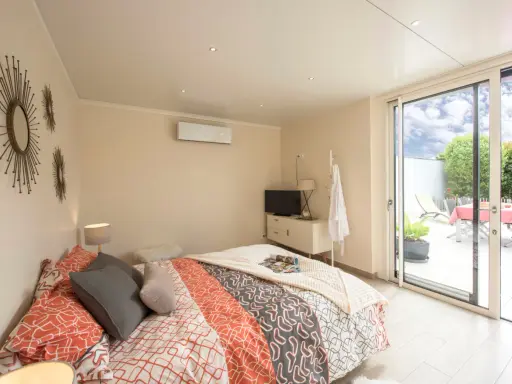 Chambre lumineuse d'une extension de maison, avec un lit confortable, une télévision et un accès direct à une terrasse extérieure.