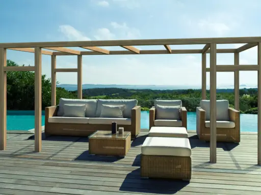 Salon extérieur avec mobilier en rotin sous une pergola en bois. La hauteur de la pergola en bois offre une ombre agréable sur la terrasse en bois, près de la piscine.