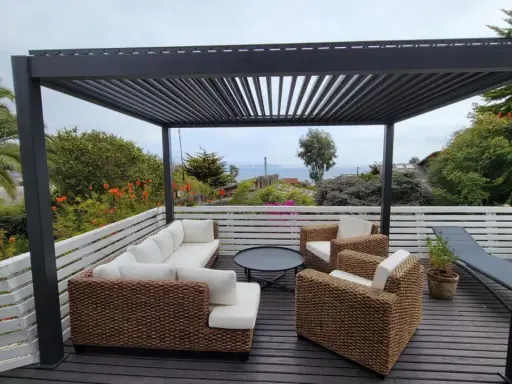 Un salon d'extérieur confortable sous une pergola sur toit terrasse, avec vue sur la mer.