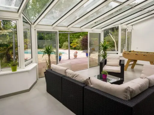 Vaste veranda 50m2 avec salon, baby-foot et vue sur piscine. Idéal pour se détendre et s'amuser en famille.