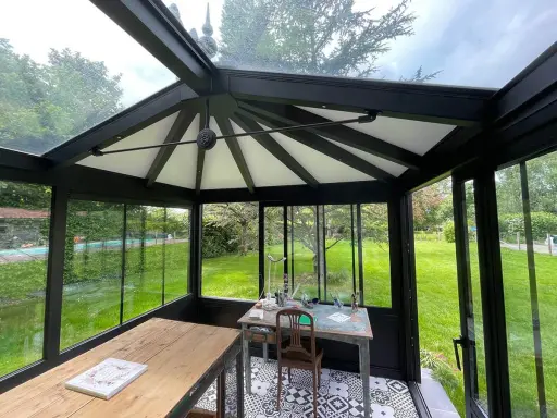 Intérieur d'une **veranda 2 pans** avec mobilier, sol décoratif et vue sur un jardin verdoyant.