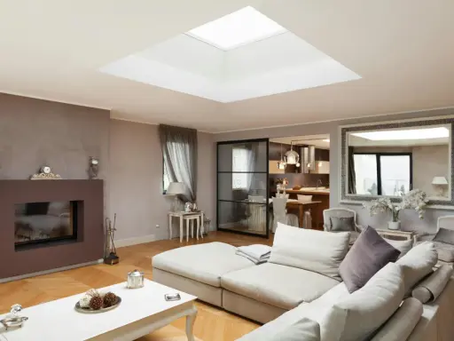 Un salon moderne avec un grand puit de lumière au plafond, un canapé confortable, une cheminée et une cuisine ouverte.