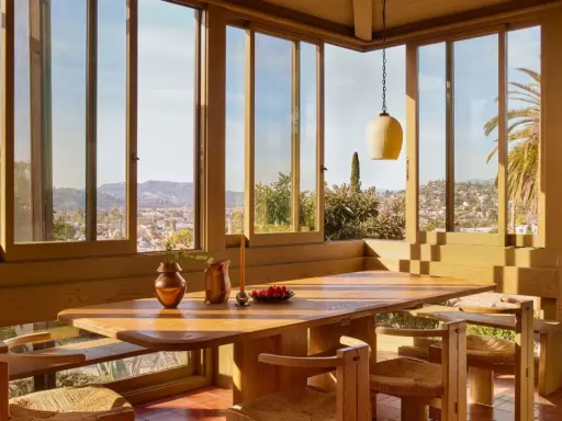 Une salle à manger lumineuse dans une veranda sur terrasse en bois, avec vue panoramique sur la ville et les palmiers.