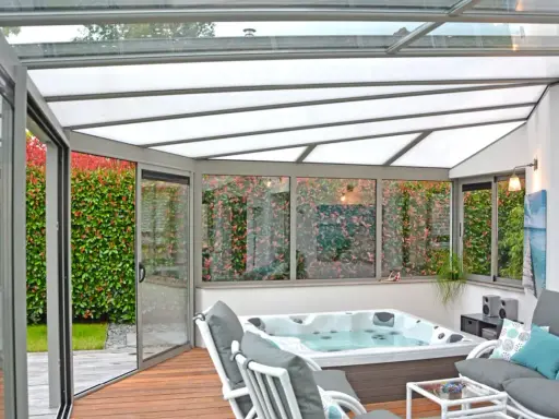 Une **fenêtre de toit veranda** lumineuse abrite un jacuzzi et un coin salon confortable, avec vue sur un jardin luxuriant.