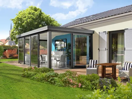 Une élégante veranda independante de la maison, avec une salle à manger et un salon d'extérieur, entourée d'un jardin verdoyant.