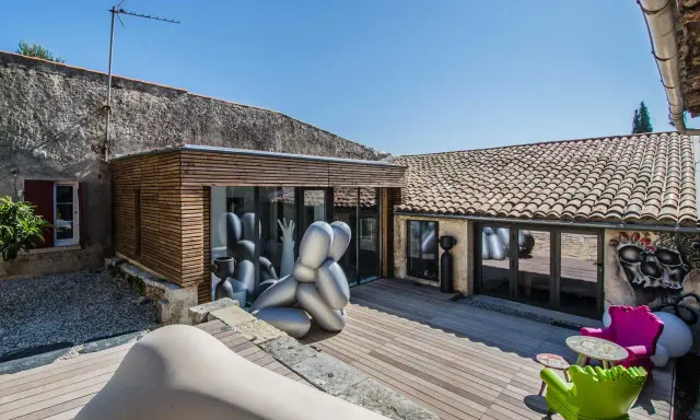 Extension maison ancienne architecte : une cour avec sculptures modernes, mobilier coloré et une extension en bois et verre.