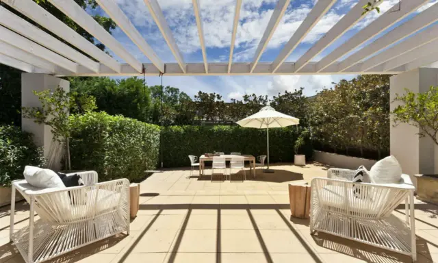 Terrasse couverte avec pergola blanche, mobilier de jardin blanc, table et parasol. Un espace extérieur aménagé, peut-être pour fermer une terrasse couverte sans autorisation.