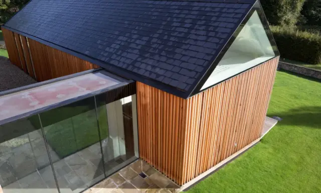 Vue aérienne d'un agrandissement maison sur le côté, avec bardage bois, toit en ardoises et extension vitrée.