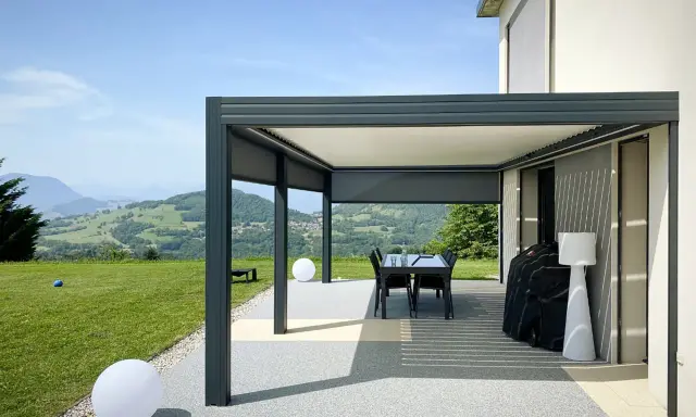 Pergola bioclimatique moderne face à un paysage vallonné. Le vent fort fait onduler les lames du toit, créant des jeux d'ombre et de lumière.