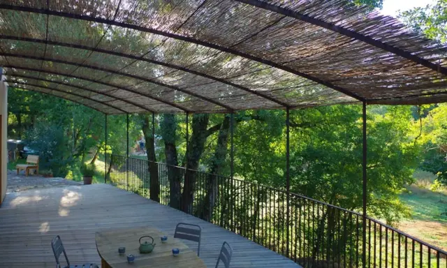 Vue d'une terrasse en bois sous une pergola recouverte de canisse. Le sens de pose de canisse sur pergola offre une ombre naturelle et agréable.