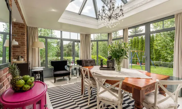 Une élégante veranda couloir avec un lustre, une table en bois et des fauteuils, donnant sur un jardin verdoyant.
