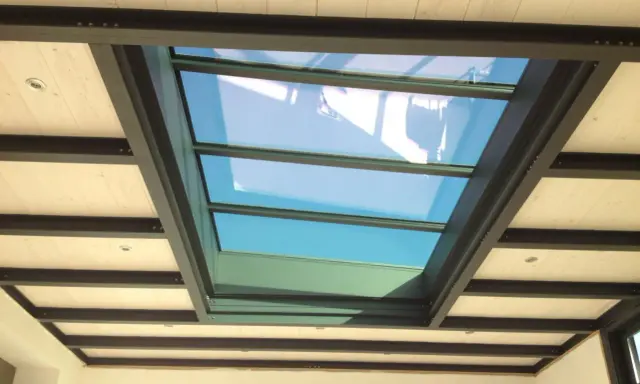 Veranda avec un grand puit de lumière vitré, illuminant un plafond en bois et poutres métalliques.