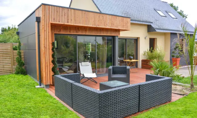 Une extension bois 30m2 moderne avec terrasse en bois, mobilier de jardin et grandes baies vitrées.