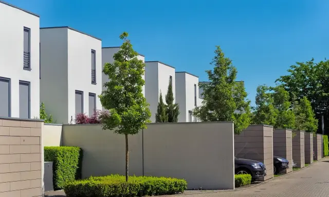 Lignes architecturales modernes, une extension accolée sur mur non mitoyen, des arbres et des voitures garées dans des box.