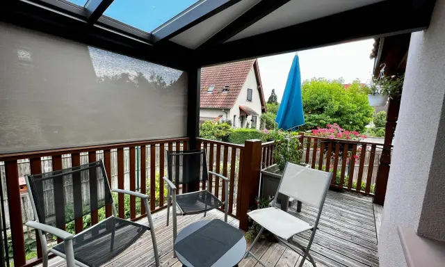 Un petit veranda balcon avec des chaises et une table, offrant une vue sur un jardin verdoyant et une maison.