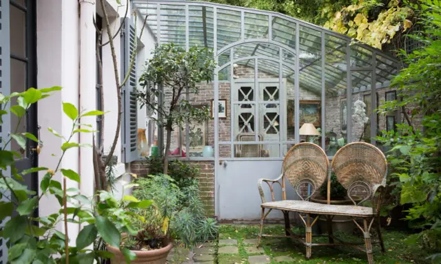 Une charmante veranda en fer forgé abrite un banc en rotin et des plantes luxuriantes, invitant à la détente dans ce jardin secret.