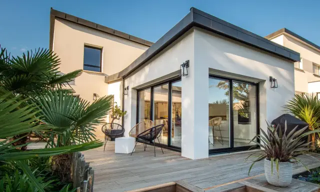 Une extension verrière moderne illumine cette maison ancienne, offrant une vue imprenable sur la terrasse en bois et le jardin luxuriant.