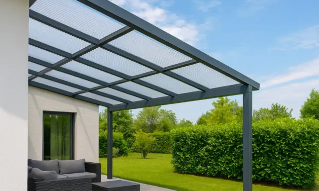 Une pergola moderne avec toit en polycarbonate protège un salon de jardin. Le ciel bleu et la verdure environnante créent un cadre paisible.