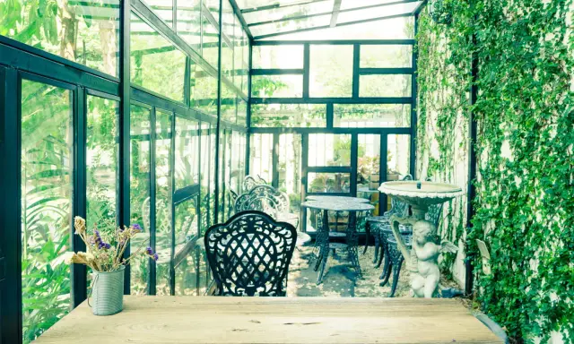 Un charmant jardin d'hiver verrière, avec des tables et chaises en fer forgé, une statue d'ange et une profusion de verdure.