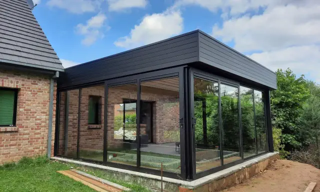 Moderne véranda toit plat avec puits de lumière, offrant une vue panoramique sur le jardin. L'extension en verre et métal s'intègre parfaitement à la maison en briques.