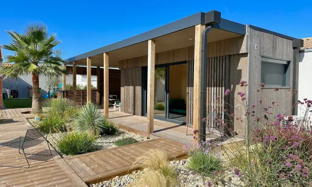 Maison moderne avec une extension toiture terrasse en bois, entourée d'un jardin paysager et d'une terrasse en bois.