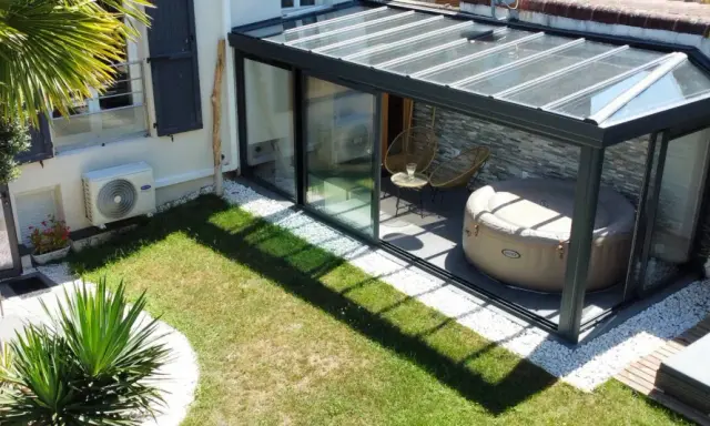 Une **veranda tuile** moderne avec jacuzzi et fauteuils, entourée d'un jardin verdoyant et d'une palme luxuriante.