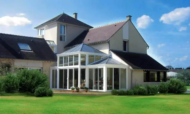 Une **veranda angle maison** moderne, avec une structure vitrée lumineuse, s'intègre parfaitement à l'architecture de la demeure.