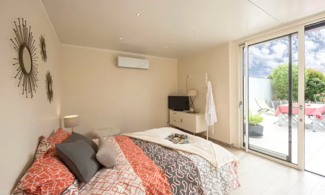 Chambre lumineuse d'une extension de maison, avec un lit confortable, une télévision et un accès direct à une terrasse extérieure.