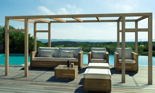 Salon extérieur avec mobilier en rotin sous une pergola en bois. La hauteur de la pergola en bois offre une ombre agréable sur la terrasse en bois, près de la piscine.