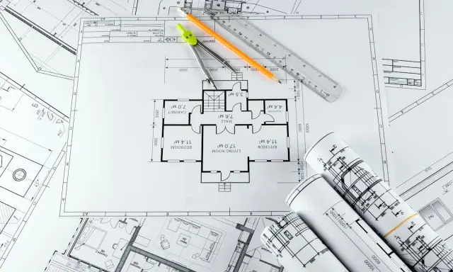 Plans d'architecte, compas, crayon et règle pour savoir comment faire une extension de maison pas chère.